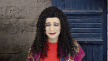 a woman with long curly hair is wearing a red shirt and a purple scarf