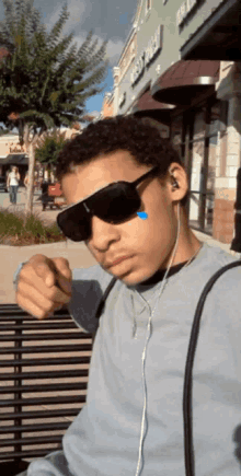 a young man wearing sunglasses and ear buds is sitting on a bench in front of a store called best buy