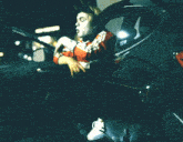 a man in a red and white sweatshirt is getting out of a car with the door open