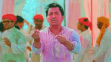 a man in a pink shirt is standing in front of a crowd with his hands in the air .