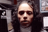 a man with curly hair is standing in front of a computer and talking .
