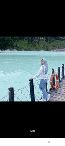 a woman in a hijab is standing on a dock near a body of water