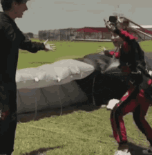 a man in a black shirt is standing next to a woman in a red suit who is jumping out of a plane .