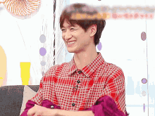 a man wearing a plaid shirt is smiling and sitting on a couch