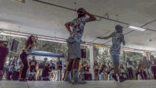 a man in a floral shirt is dancing in front of a crowd while a woman watches