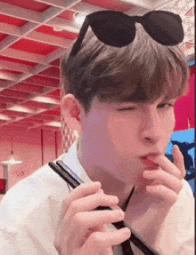 a young man wearing sunglasses is eating with chopsticks and making a funny face .