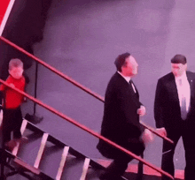 a man in a suit and tie is walking down a set of stairs with a little boy in a red shirt behind him