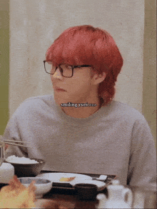 a man with red hair and glasses sits at a table with a bowl of rice in front of him