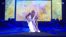 a woman in a white dress is dancing on a stage in front of a line tv screen
