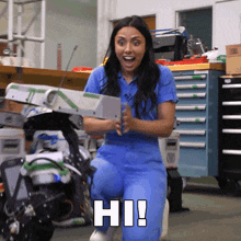 a woman in a blue jumpsuit is holding a robot and says hi!