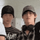 two young men wearing hats and headphones are standing next to each other and looking at the camera .