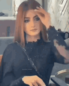 a woman in a black shirt is sitting in a chair and touching her hair .