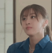 a close up of a woman 's face wearing a blue shirt and ponytail .