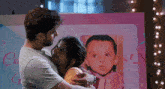 a man is hugging a woman in front of a picture of a child .