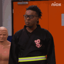 a man wearing a black shirt with a pink dragon on it is standing in front of an orange door with nick written on it