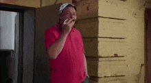 a man in a red shirt is smoking a cigarette in front of a yellow wall .
