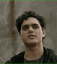 a close up of a man 's face with curly hair wearing a black jacket .