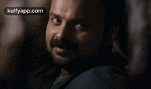 a man with a beard and mustache is looking at the camera with the words kulfyapp.com in the corner