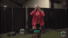 a man in a pink jacket is standing in front of a sign that says effy