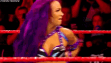 a female wrestler with purple hair is standing in a wrestling ring .