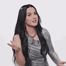a woman with long black hair is wearing a silver dress and necklace