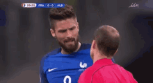 a soccer player in a blue shirt is talking to a referee in a red shirt .