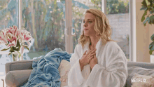 a woman in a bathrobe is sitting on a couch with a netflix logo on the bottom right