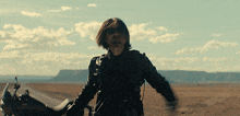 a man in a leather jacket is riding a motorcycle on a desert road