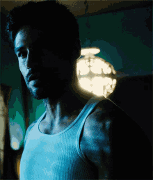 a man in a white tank top stands in front of a lamp