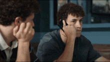 a man with curly hair is talking on a cell phone while another man looks at him