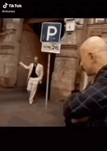 a man in a suit is standing in front of a parking sign and talking to another man .