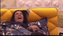 a woman is laying on a yellow couch laughing with her mouth open