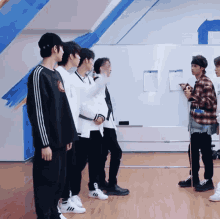 a group of young men are standing in front of a white board and one of them has the word adidas on his shoe