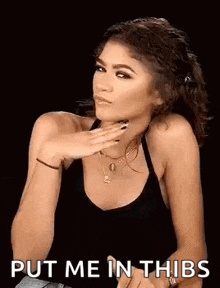 a woman in a black tank top is sitting down with her hand on her chin .