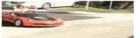 a little boy is driving a red toy car on a street .