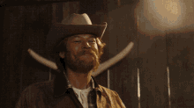 a man wearing a cowboy hat stands in front of a wall with horns on it