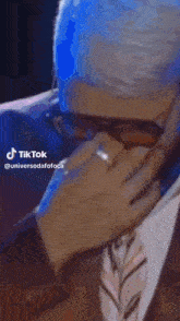 a man in a suit and tie is covering his face with his hand while talking on a cell phone .