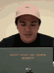 a man wearing a pink hat is looking at a laptop screen that says " kahit hindi ako broken "