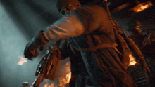 a man holding a gun in a dark room with flames behind him