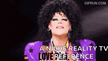 a drag queen is wearing a purple jacket and a wig and says `` a niche reality tv love reference '' .