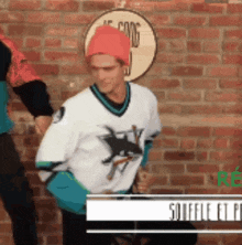 a man wearing a sharks jersey is standing in front of a brick wall
