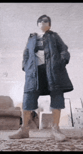 a man is standing in a living room wearing a coat and shorts .