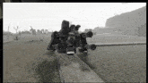 a black and white photo of a robot standing on top of a wooden plank in a field .