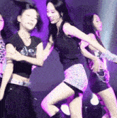 a group of young women are dancing on a stage in front of purple lights .