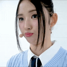 a woman wearing a blue sweater and a white shirt looks at the camera