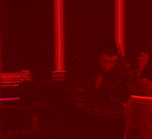 a person is standing in a dark room with red lights behind them and a statue of a city in the background .