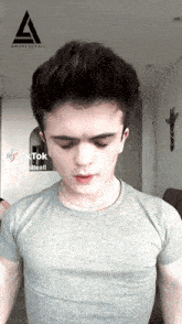 a young man wearing a grey t-shirt has a tiktok sticker on his shirt