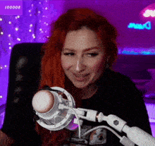 a woman with red hair is sitting in front of a microphone with a purple background behind her that says 100008