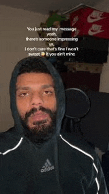 a man with a beard wearing a hoodie is standing in front of a microphone in a room .