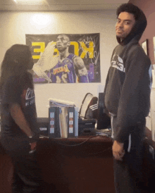 a man and a woman are standing in front of a poster of kobe bryant